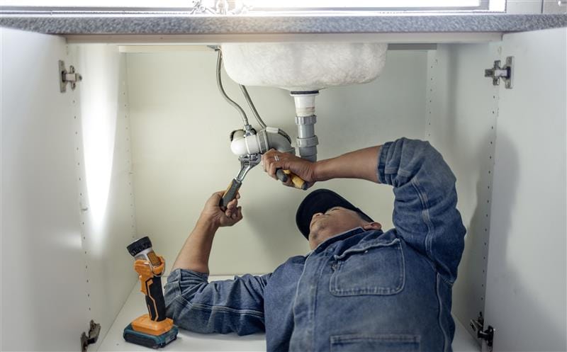 Plumber repairing pipes beneath a bathroom sink in Redwood City
